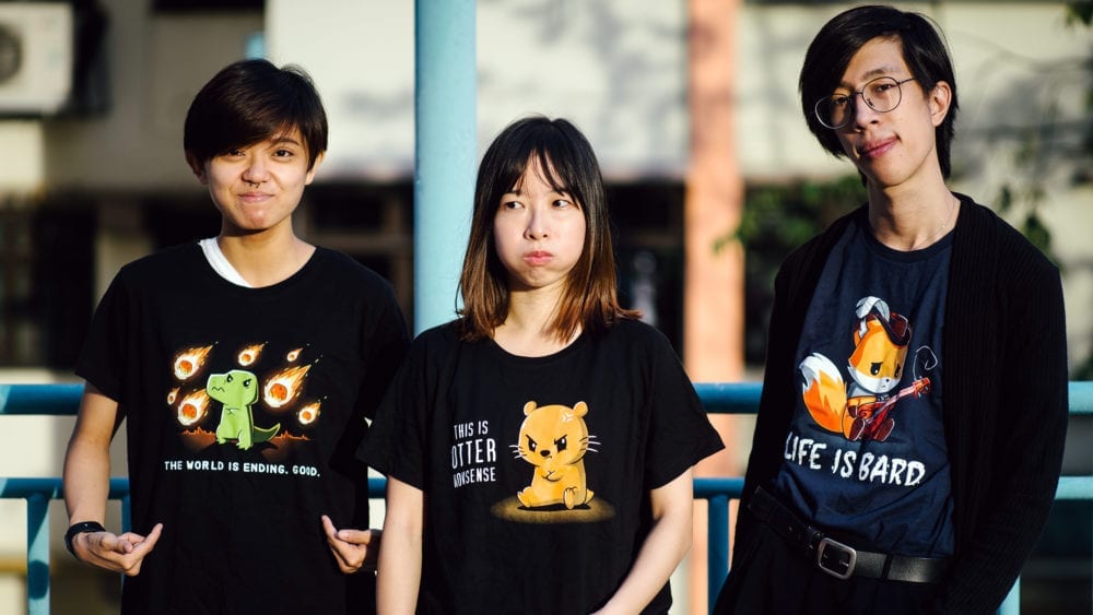 three young people wearing black t-shirts, each with colourful and comical prints on the front
