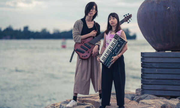 Altoduo standing on rocks holding their instruments at the Singapore Harbour